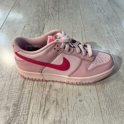 Vu de coté de la paire de Nike dunk low triple pink. Différentes teintes de rose. Un. logo nike rose foncé. Des lacets rose clair.