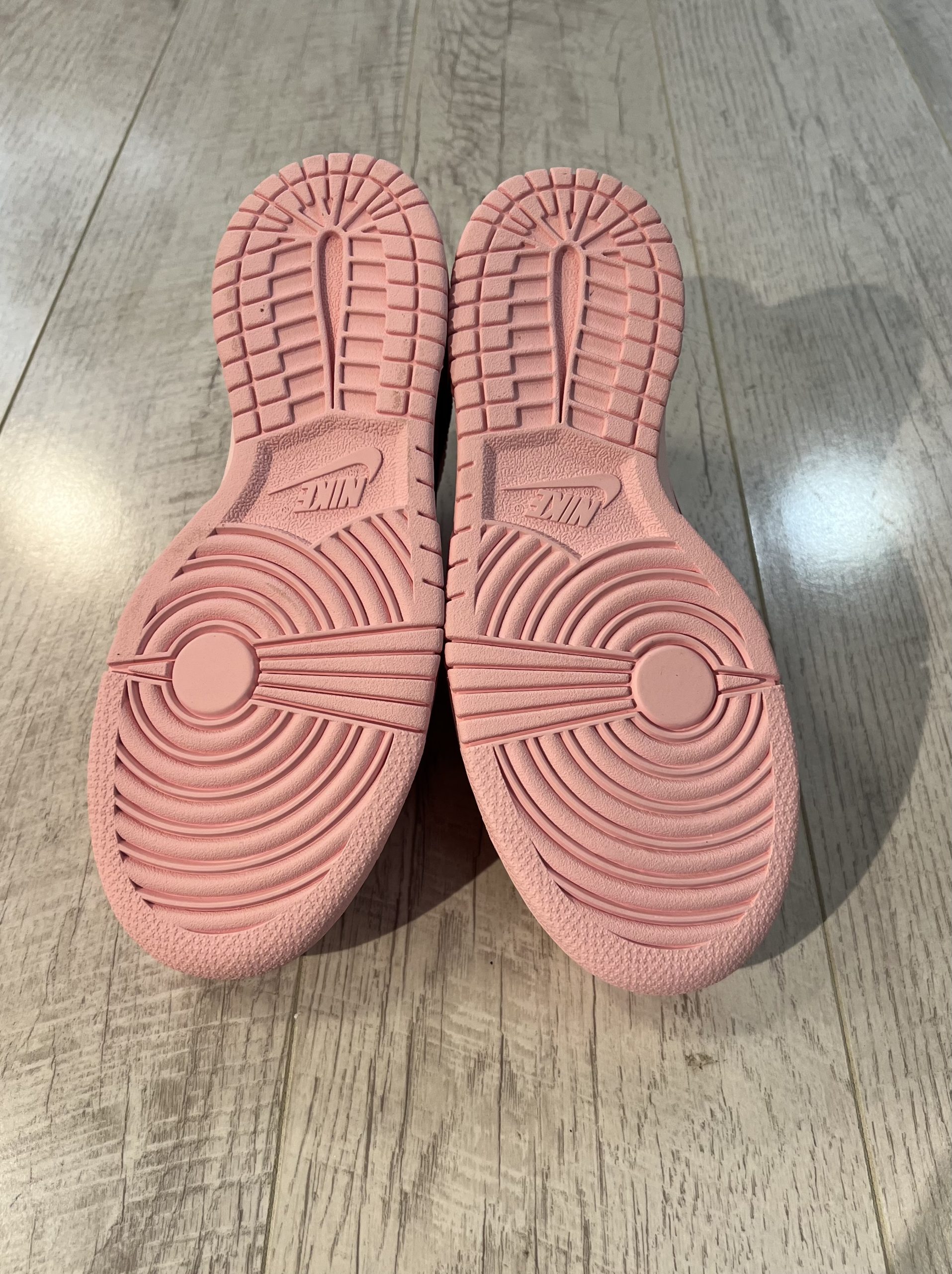 nike-dunk-low-triple-pink.jpeg Vu du dessous de la paire de Nike dunk low triple pink. La couleur rose domine la semelle de la paire.