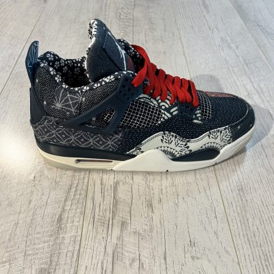 Vu de coté de la paire de Nike Jordan 4 SE Deep Ocean. Une couleur effet jeans est présente de couleur bleu avec quelques touches de rouges Des lacets rouges sur la chaussure. Une semelle blanche.