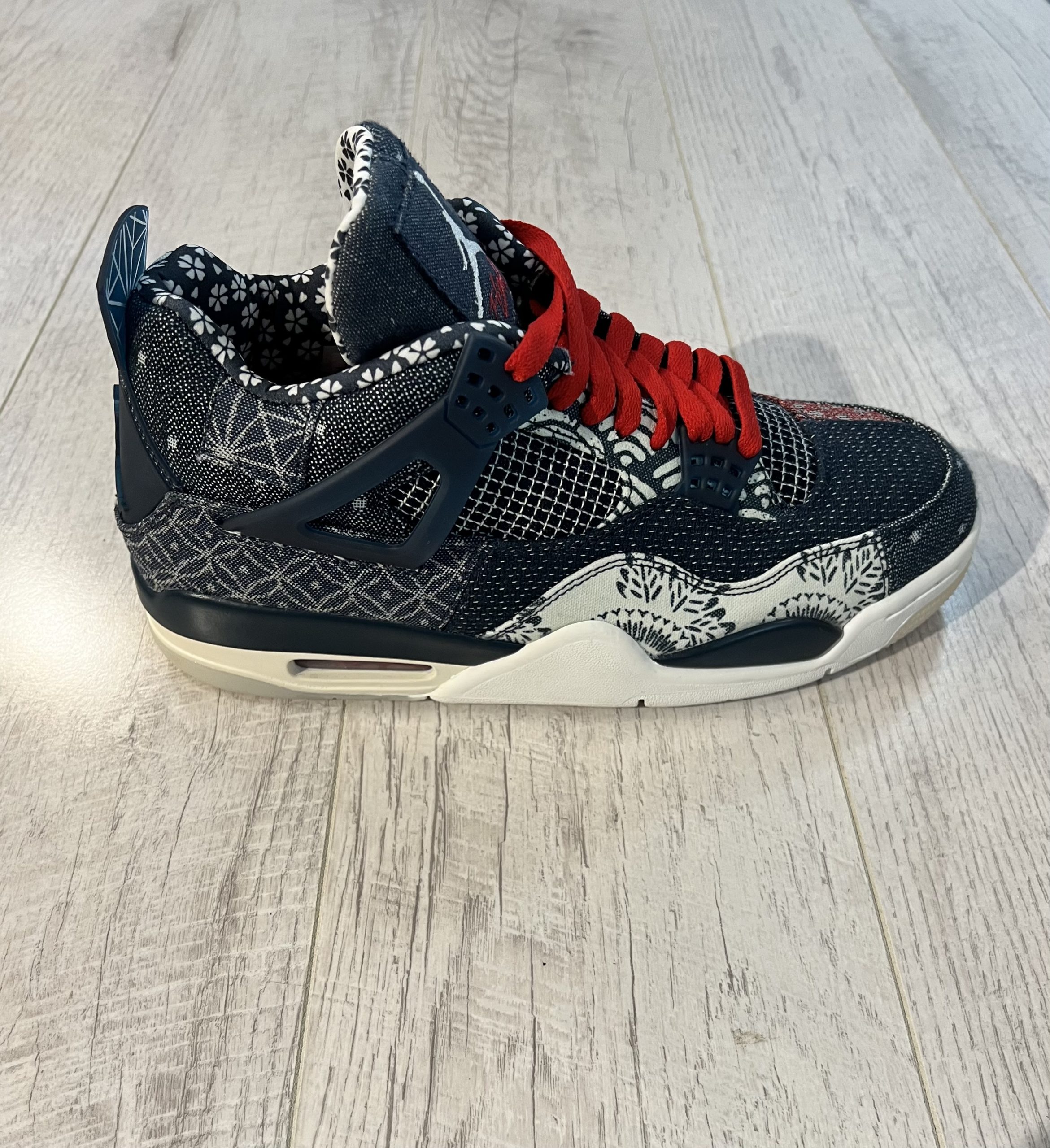 nike-air-jordan-4-se-deep-ocean.jpeg Vu de coté de la paire de Nike Jordan 4 SE Deep Ocean. Une couleur effet jeans est présente de couleur bleu avec quelques touches de rouges Des lacets rouges sur la chaussure. Une semelle blanche.