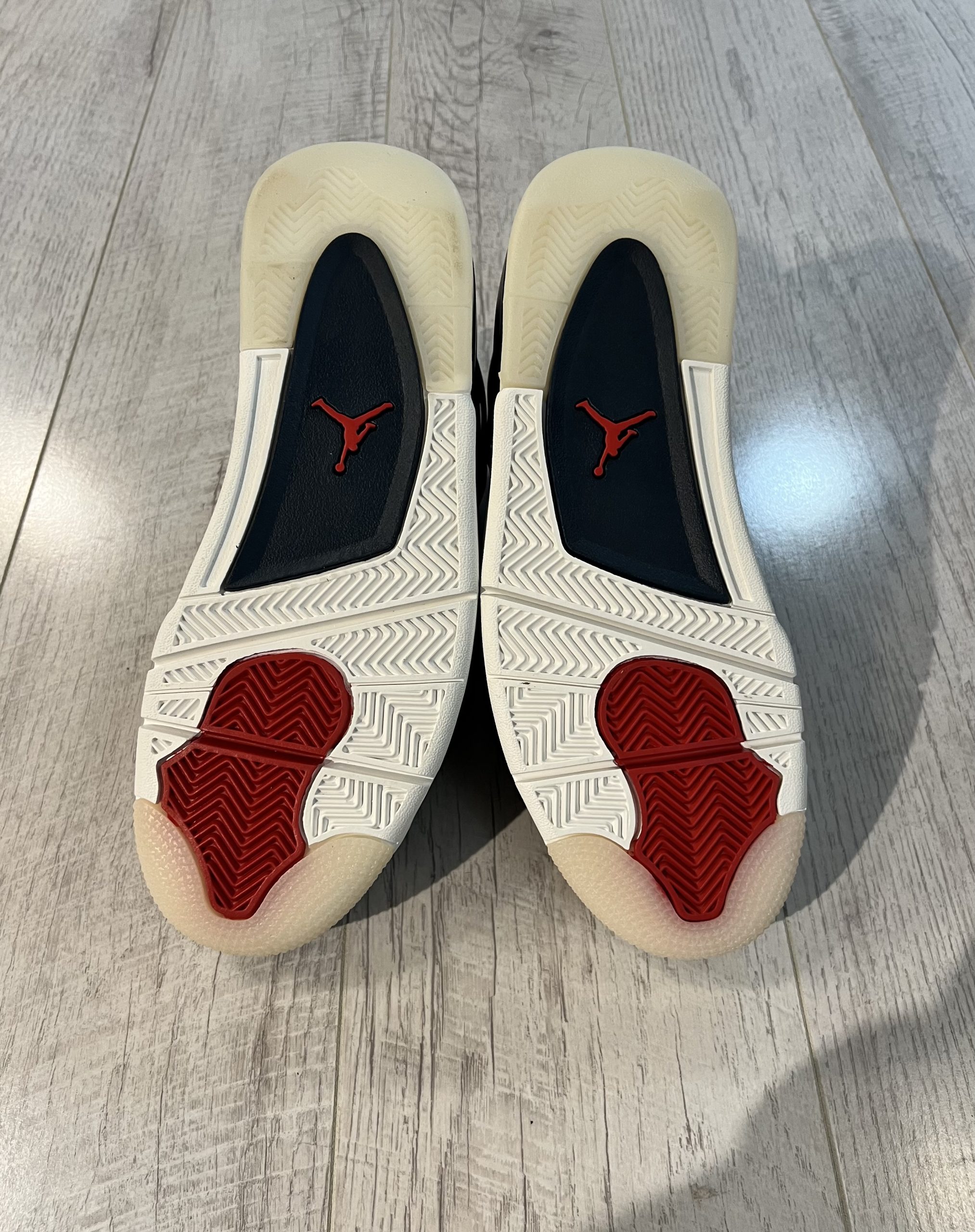 nike-jordan-4-se-deep-ocean.jpeg Vu du dessous de la Nike Jordan 4 SE Deep Ocean. Du blanc domine, une touche de rouge et de beige. Du noir au milieu de la semelle avec un logo jordan rouge.