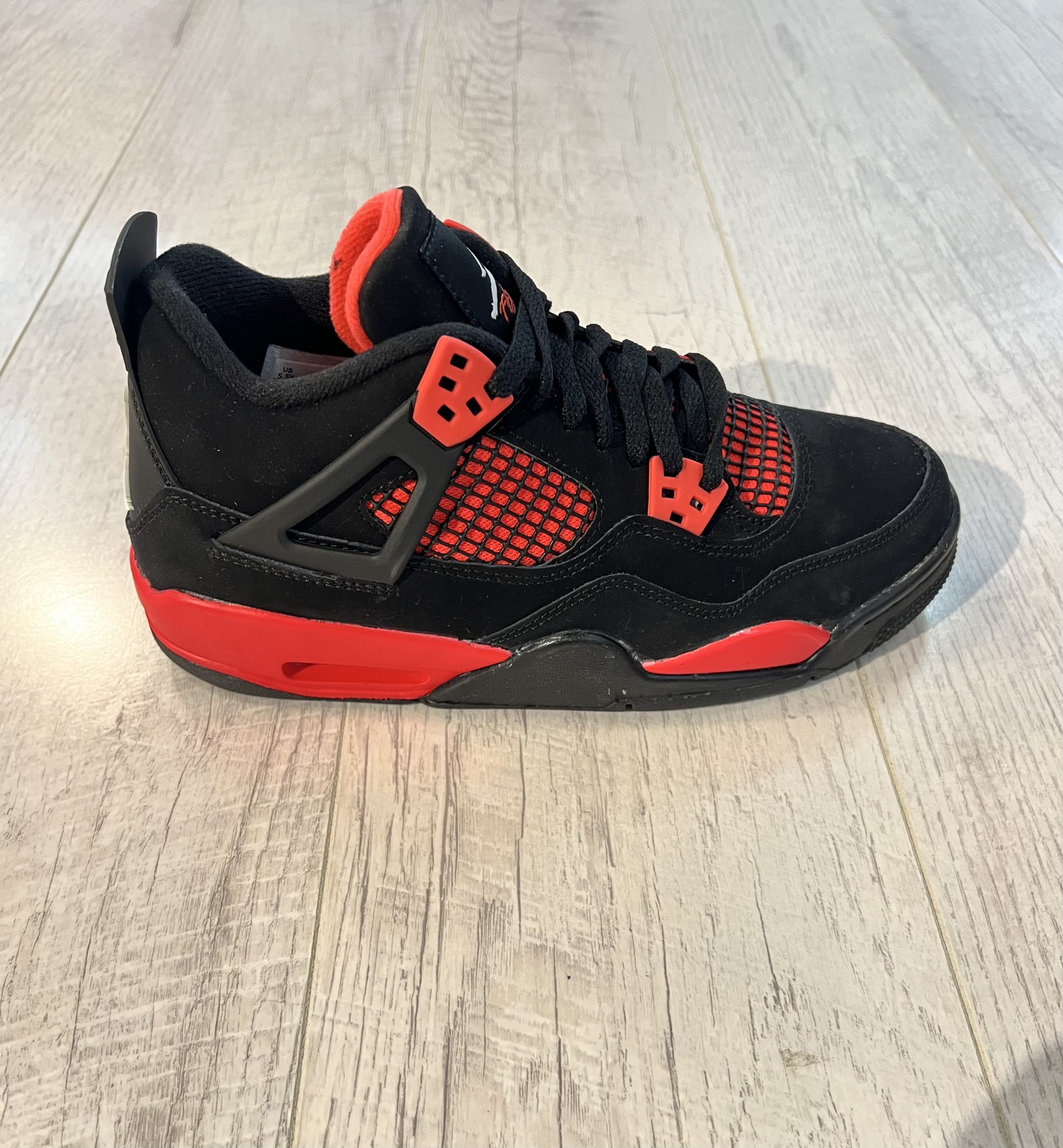nike-air-jordan-4-red-thunder.jpeg Vu de coté de la Nike Air Jordan 4 Red Thunder. Du noir et du rouge sur la paire. Un logo jordan blanc sur la languette.