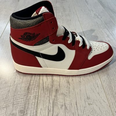Vu de coté de la Nike Air Jordan 1 High OG Lost and Found. Le rouge et le blanc dominent. Un swoosh nike noir, une languette beige, des lacets noirs et blancs. L'intérieur de la paire est noir.