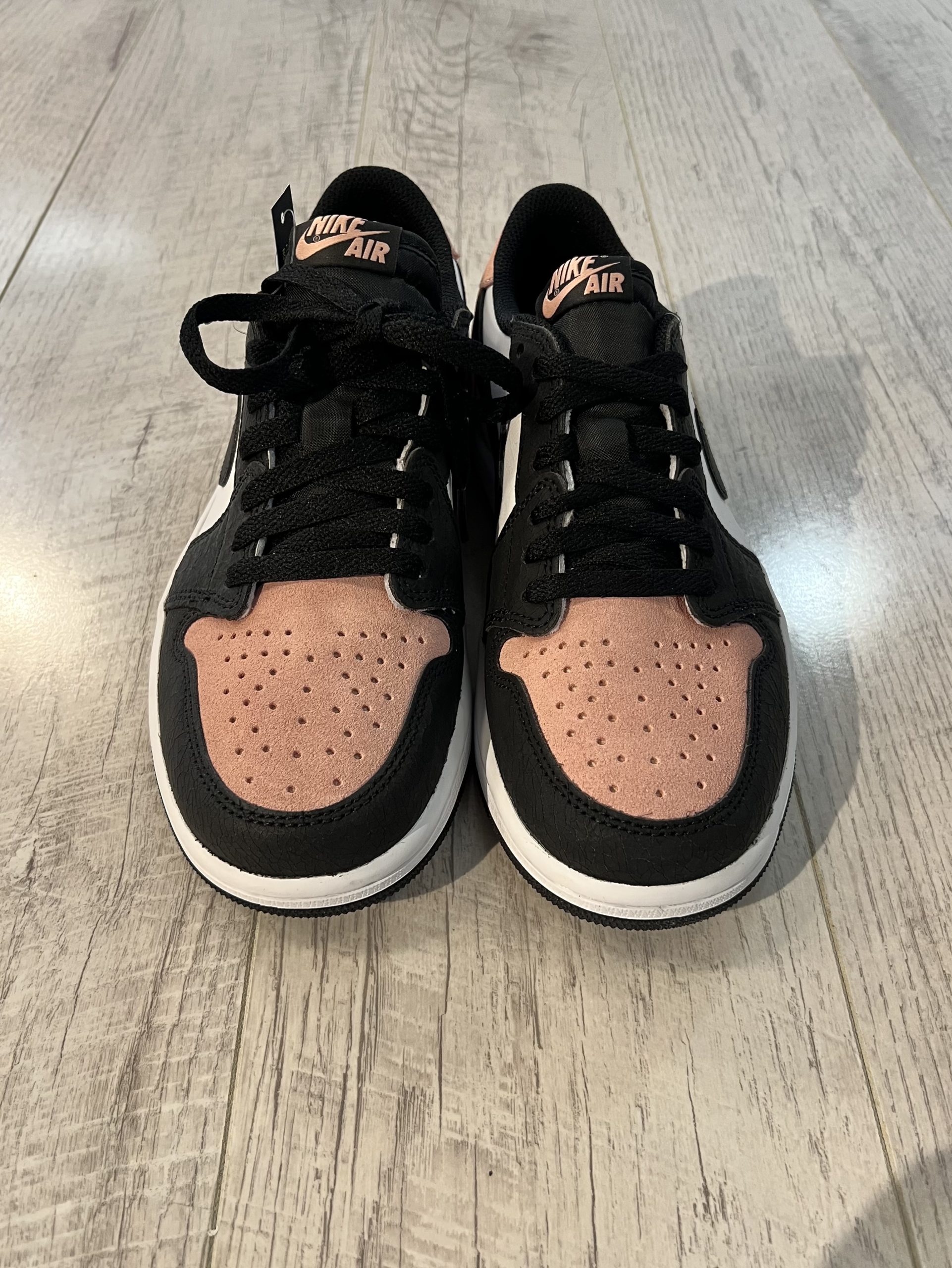 nike-air-jordan-1-low-og-bleached-coral.jpeg Vu du dessus de la Nike Air Jordan 1 Low OG Bleached Coral. Du noir domine la paire ainsi qu'un rose pastel en daim.