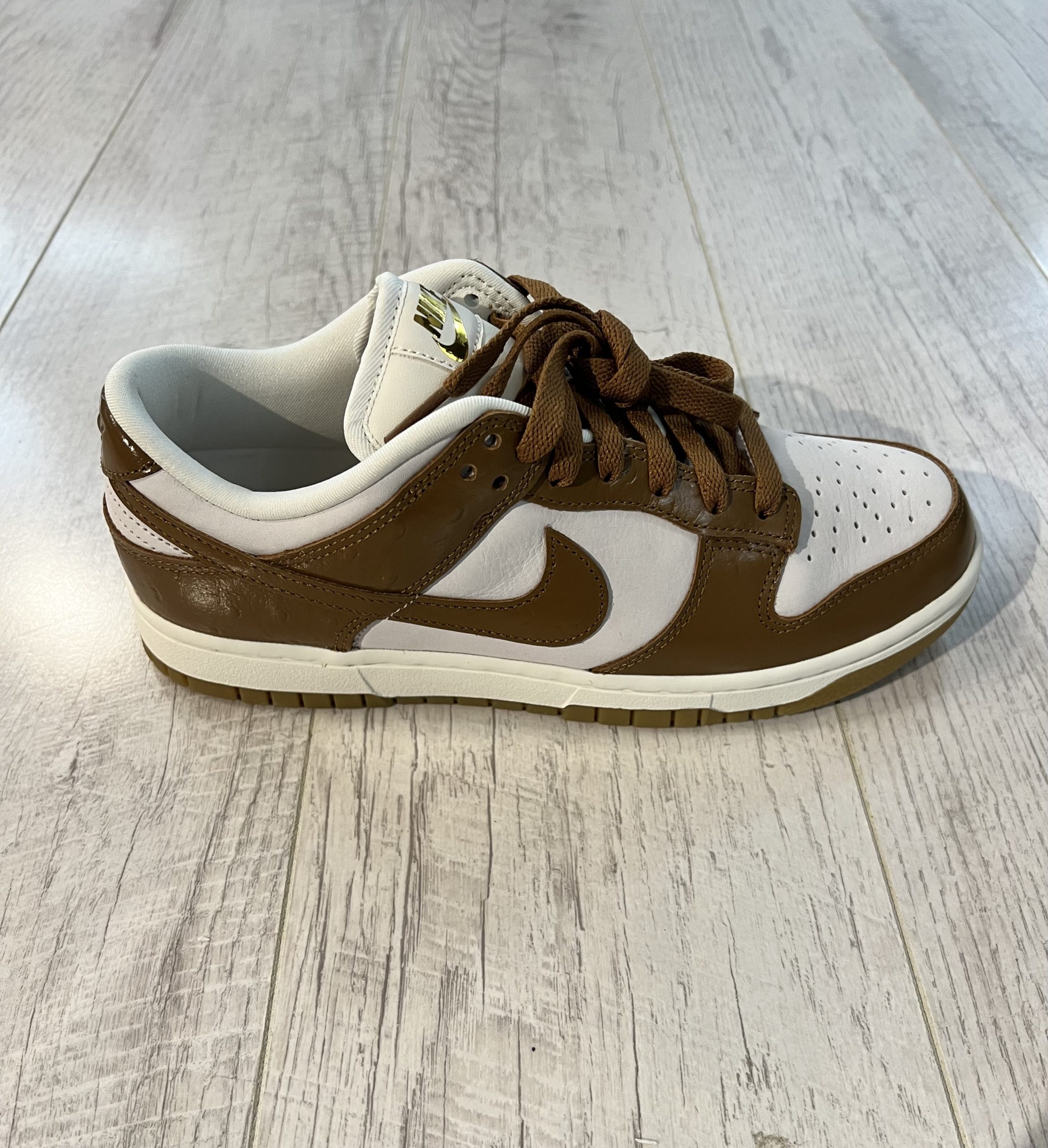 nike-dunk-low-lx.jpeg Vu de coté de la paire de Nike Dunk Low LX. Le marron domine le dessus de la paire. Du blanc est present. Les lacets sont marrons.