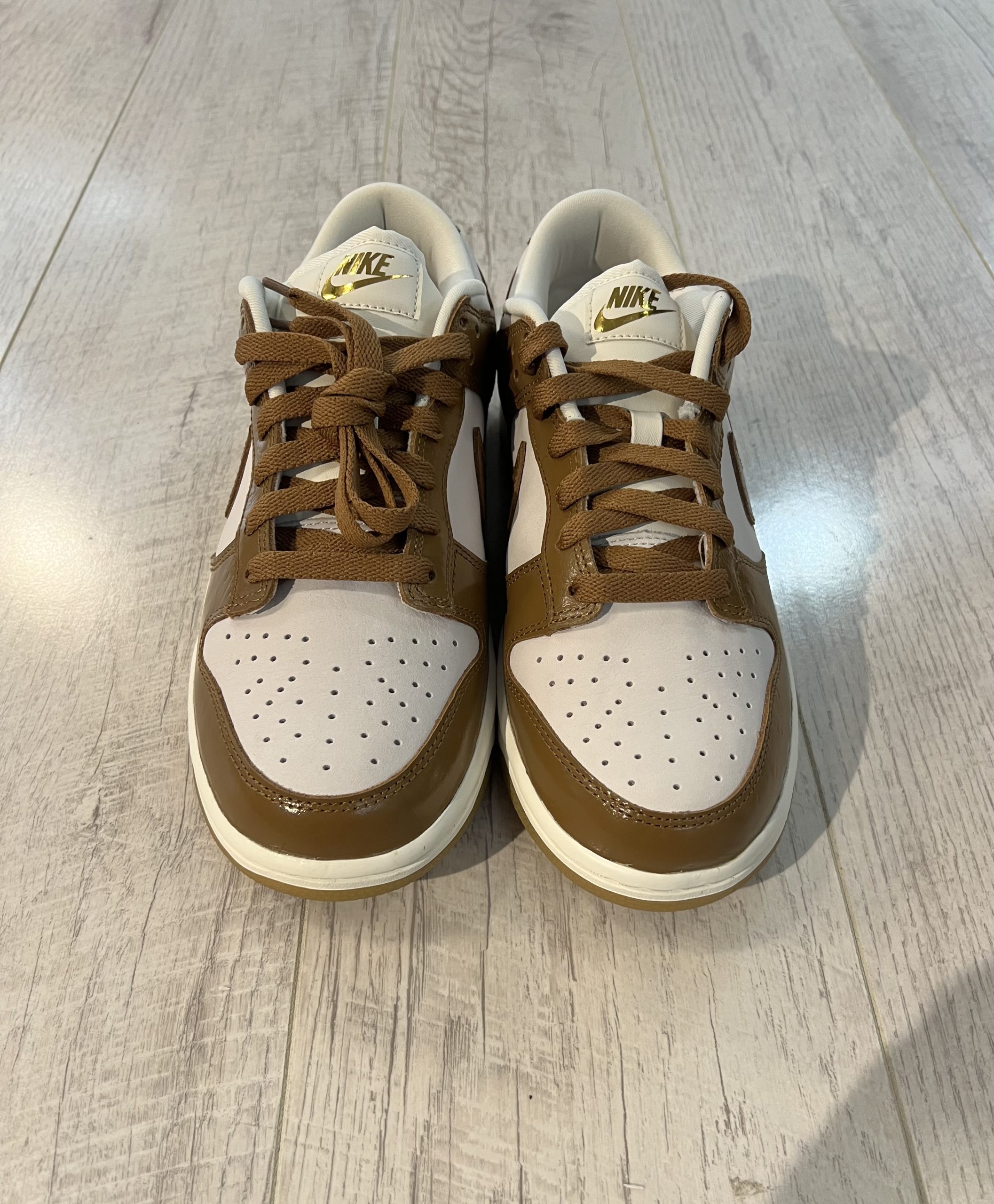 nike-dunk-low-lx.jpeg Vu du dessus de la paire de Nike Dunk Low LX. Le marron domine le dessus de la paire. Du blanc est present. Les lacets sont marrons.