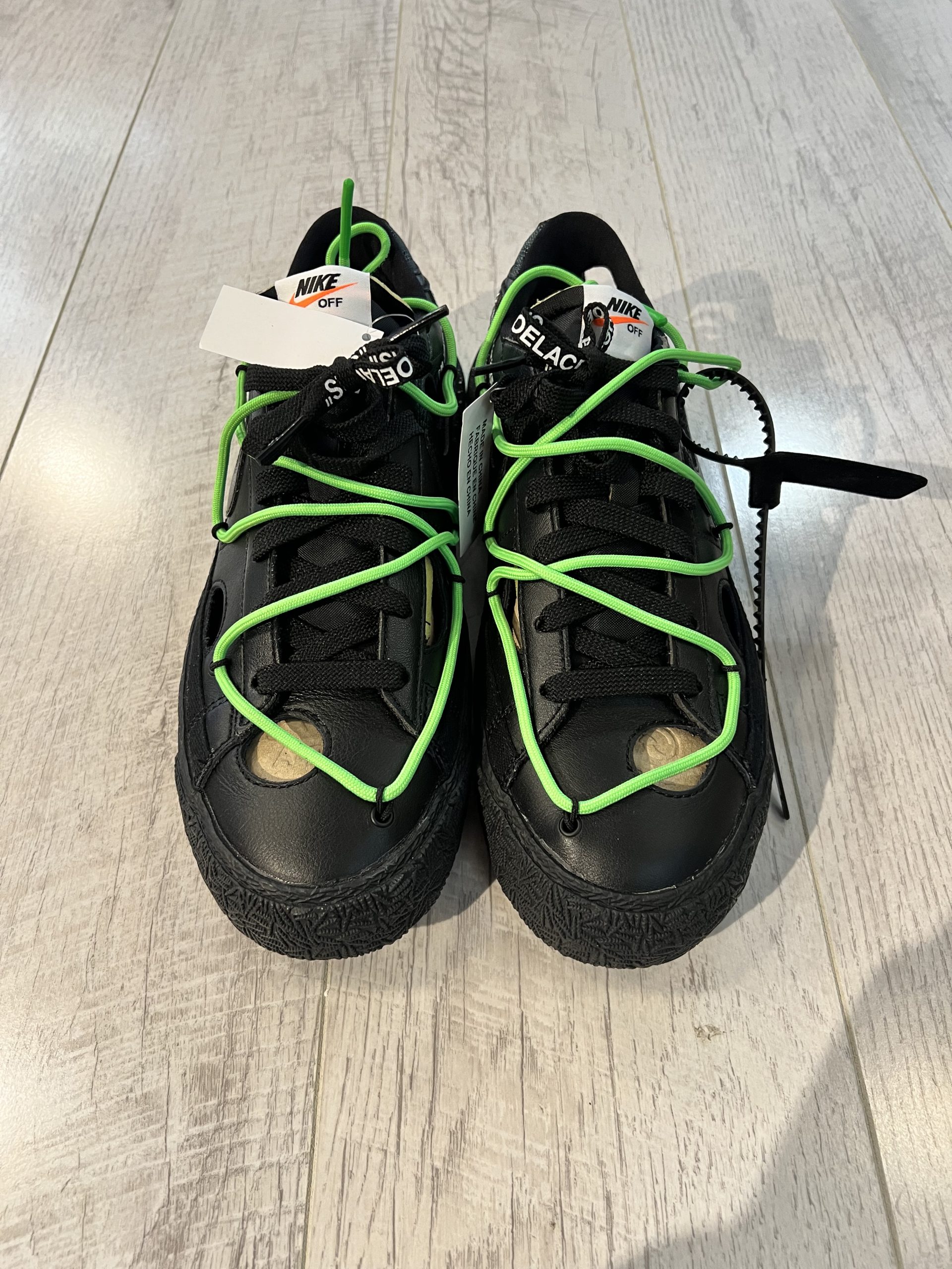 nike-blazer-low-off-white-black-.jpeg Vu du dessus de la paire de Nike Blazer Low OFF White Black. Le noir domine la paire. Un lacet vert est sur le dessus de la paire. Des lacets noirs